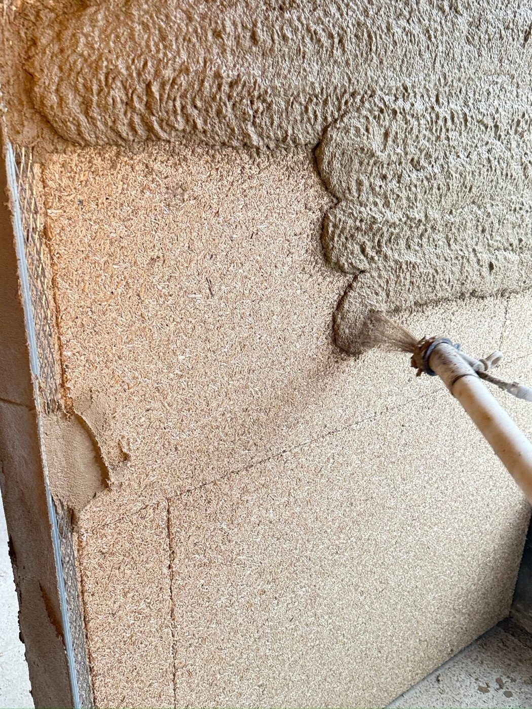 Hemp-lime plaster being spray-applied over a mesh substrate on a HEMPLITH wall panel